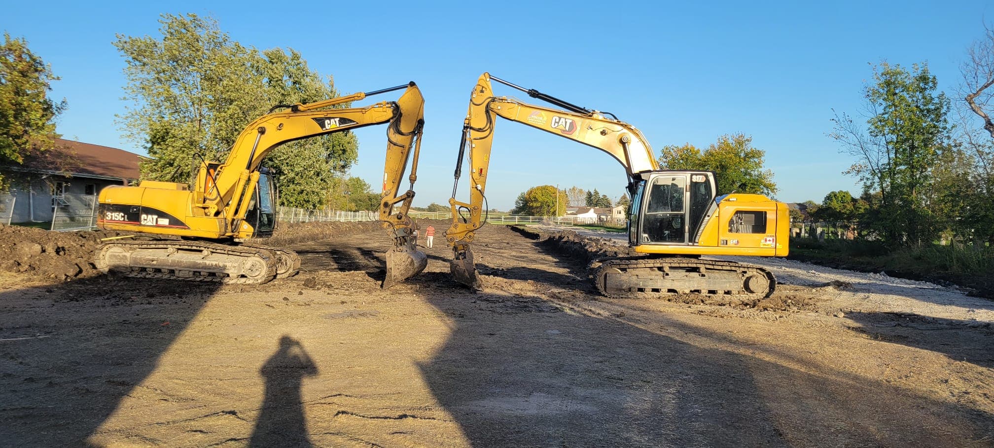 Two yellow CAT excavators face each other with buckets touching on a dirt construction site.